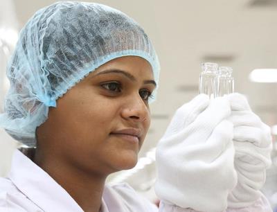 Eine Mitarbeiterin kontrolliert zwei Glasfläschchen in der Schott Kaisha Produktion im indischen Jambusar